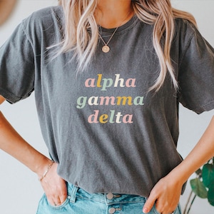 May include: A gray t-shirt with the text "alpha gamma delta" in pastel colors.