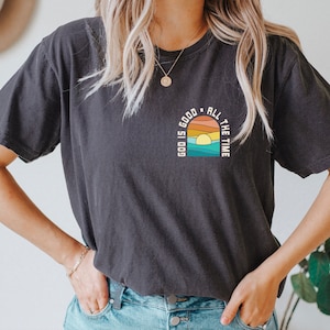 May include: A black t-shirt with a graphic design of a sunset over water with the text "God is good all the time".