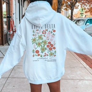 May include: White hooded sweatshirt with a floral design and the text "Kappa Delta Established 1997 October 23 Building Confidence Inspiring Action"