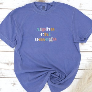 Pu&ograve; includere: Una maglietta blu a maniche corte con la scritta "Alpha Chi Omega" stampata in lettere colorate.