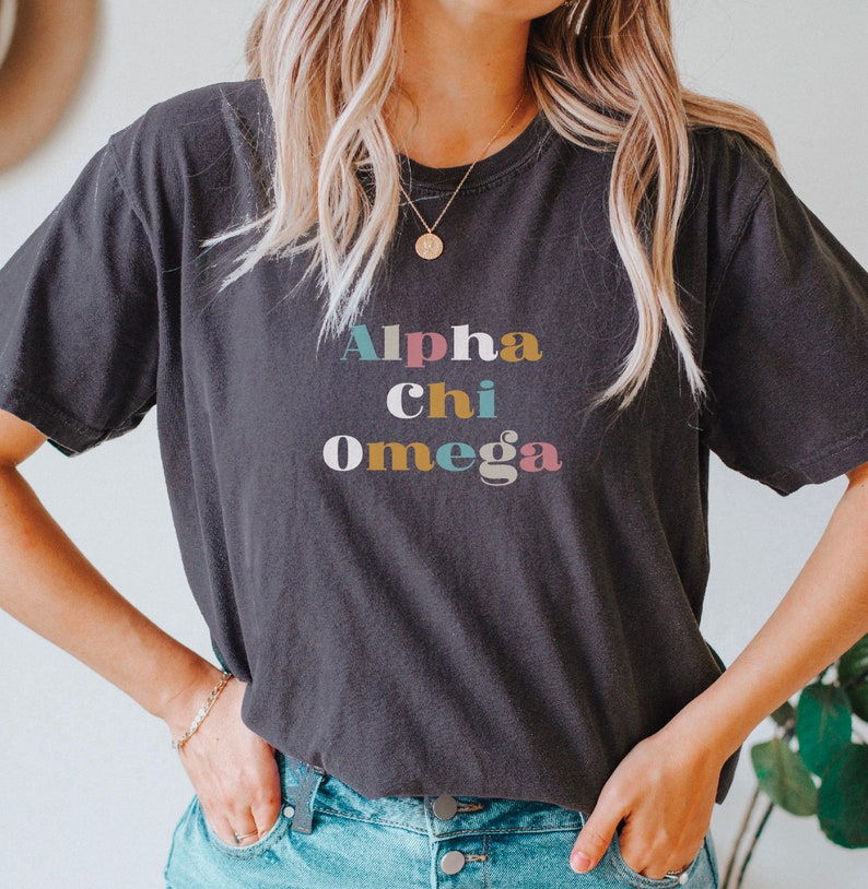 Pu&ograve; includere: Una maglietta nera con il testo "Alpha Chi Omega" in lettere colorate.