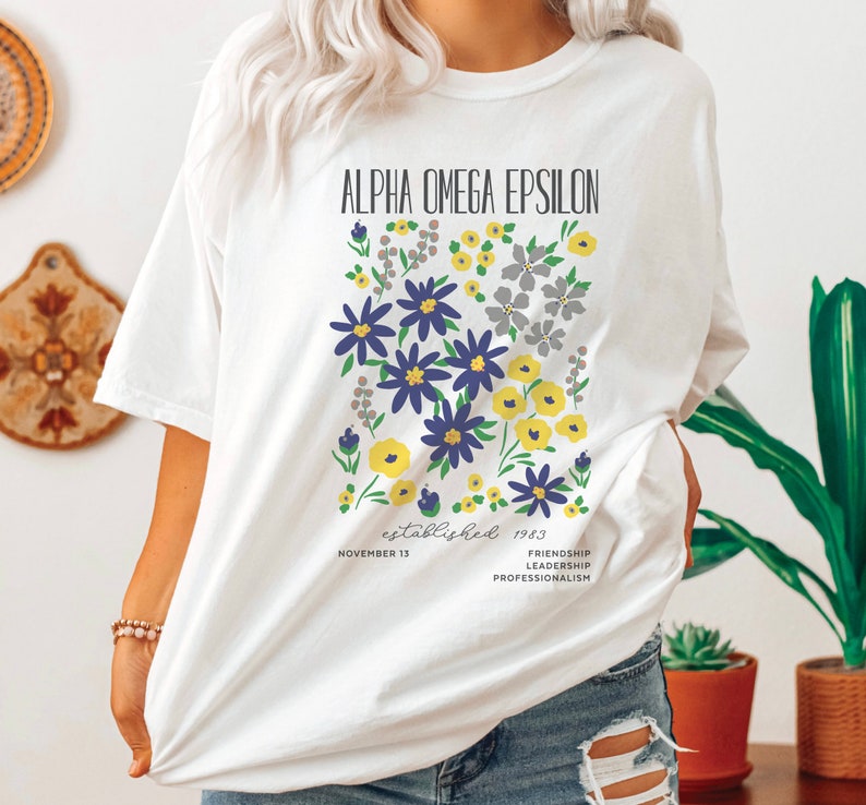 May include: White t-shirt with a floral design and the text "Alpha Omega Epsilon established 1983 November 13 Friendship Leadership Professionalism".