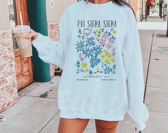May include: White sweatshirt with a floral design and the text "PHI SIGMA SIGMA established 1913 NOVEMBER 26 DIKETE NURPSALA".