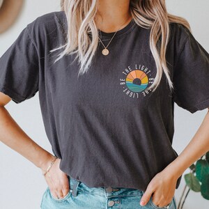 May include: A black t-shirt with a graphic of a sunset and the text "Be the light. Be the light." in a circle.