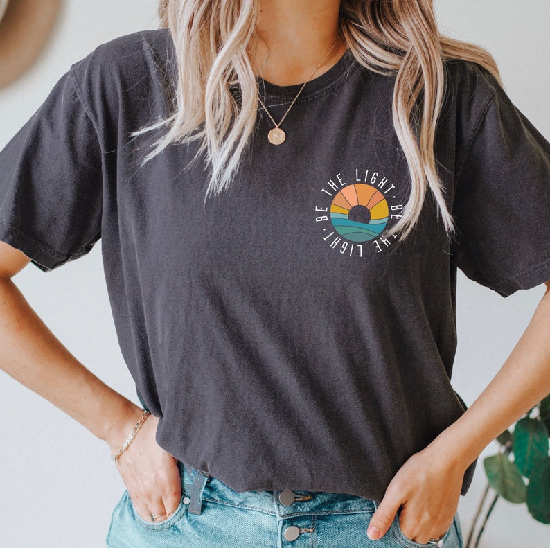 May include: A black t-shirt with a graphic of a sunset and the text "Be the light. Be the light." in a circle.