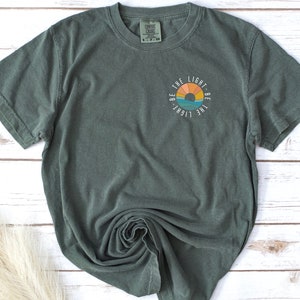 May include: A green t-shirt with a graphic of a sunset and the text "Be the light. Be the light."