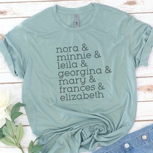 May include: A light blue t-shirt with the text "nora & minnie & leila & georgina & mary & frances & elizabeth" printed on the front.