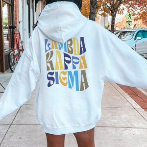 Peut inclure: Sweat-shirt à capuche blanc avec un graphique coloré "Lambda Kappa Sigma" au dos.