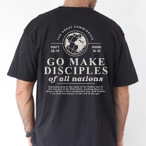 May include: Black t-shirt with white text and a globe graphic. The text reads "GO MAKE DISCIPLES of all nations" with references to Matthew 28:19 and Mark 16:15. The shirt also includes a quote about baptism and teaching.