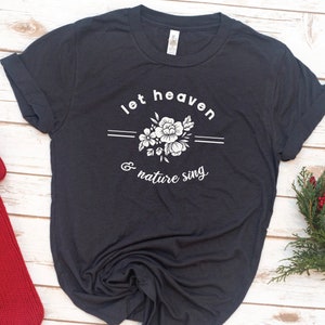 May include: A dark gray t-shirt with a white floral design and the text "let heaven & nature sing".
