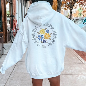 May include: White hooded sweatshirt with a circular graphic on the back. The graphic features the text "Lambda Kappa Sigma" in a circle with a floral design in the center. The text "Est. 1913" is below the circle.