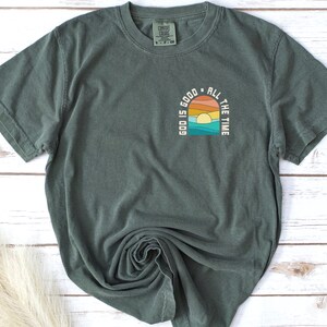 May include: A dark green t-shirt with a graphic print of a sunset and the text "Good is good all the time".