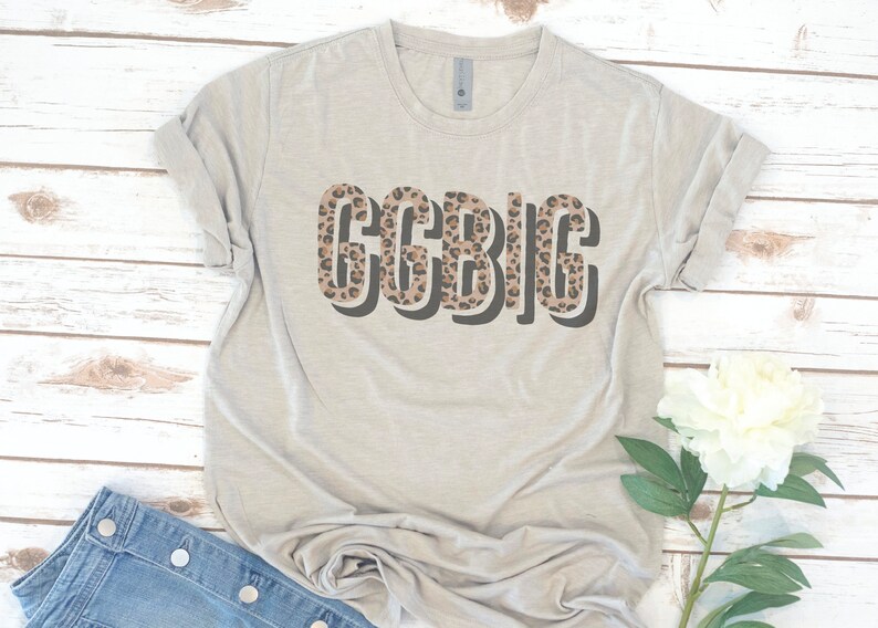 May include: A light gray t-shirt with a leopard print design that says "GCBIG" in bold, black letters.