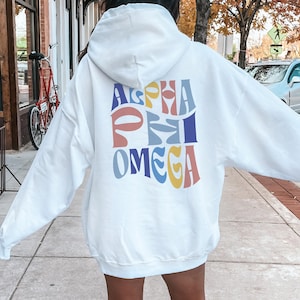Puede incluir: Sudadera con capucha blanca con un gráfico colorido de "Alpha Phi Omega" en la espalda.