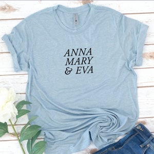 May include: A light blue t-shirt with the text "ANNA MARY & EVA" printed in black.