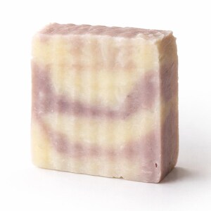 Puede incluir: Una pastilla rectangular de jabón artesanal con un diseño en capas. El jabón presenta bandas alternas de colores amarillo claro y lavanda. El jabón es un bloque sólido, con una superficie ligeramente texturizada.