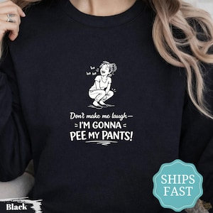 May include: A black crewneck sweatshirt featuring a white graphic of a person crouching and laughing with the text "ha ha ha" above them. Below the graphic, the text reads "Don't make me laugh—I'M GONNA PEE MY PANTS!" in a bold, white font.