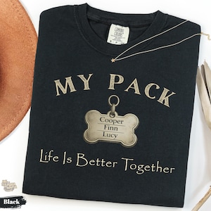 Może przedstawiać: Czarny t-shirt z okrągłym dekoltem z napisem MY PACK w jasnobrązowej czcionce nad grafiką w kształcie kości z imionami Cooper, Finn i Lucy. Poniżej zawieszki znajduje się napis Life Is Better Together wydrukowany w kolorze jasnobrązowym.