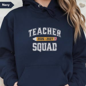 May include: Navy blue hoodie featuring the text "TEACHER SQUAD 2026-2027" in white, with a yellow and pink pencil graphic. The hoodie has a drawstring hood and a front pocket. The word "Navy" is in the upper left corner.