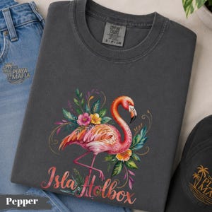 May include: A dark gray t-shirt featuring a watercolor flamingo design with the text "Isla Holbox". The flamingo is pink and orange, surrounded by colorful flowers and green leaves. The shirt is labeled "Pepper".