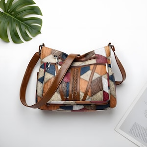 May include: A patchwork crossbody bag in various colours, with brown leather straps and detailing. The bag features geometric shapes in shades of brown, blue, red, and white. It has multiple zipped compartments and a braided detail.