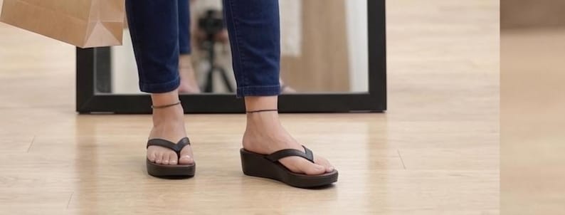 Op de afbeelding: Bruine leren sleehak sandalen met een teenslipper ontwerp. De sandalen hebben een plateauzool en worden gedragen met een donkerblauwe jeans. Een bruine papieren boodschappentas is zichtbaar.
