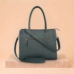 May include: A dark green rectangular handbag featuring two top handles and a detachable shoulder strap. The front of the bag includes a horizontal zippered pocket with a matching pull tab, and the overall design is structured with clean lines.