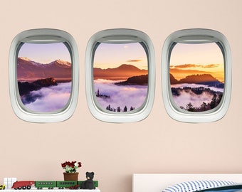 May include: Three airplane window decals featuring scenic views of mountains and clouds. The decals are white with a grey border and are arranged horizontally on a light pink wall.