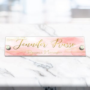 May include: A pink and gold acrylic desk nameplate with the text "Jennifer Russo - Project Manager".