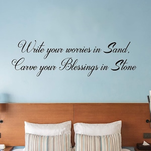 May include: A bedroom with a wooden headboard and two pillows. The wall behind the headboard has a black vinyl wall decal with the quote "Write your worries in sand, carve your blessings in stone."
