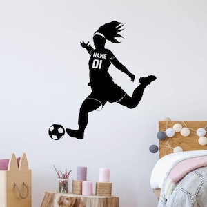 May include: Black silhouette of a soccer player kicking a soccer ball. The player is wearing a jersey with the number 01 and the word "NAME". The image is a wall decal.