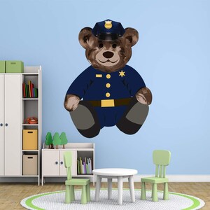 May include: A brown teddy bear wearing a blue police officer uniform with a gold badge and a blue hat with a gold star. The bear is sitting on a light blue wall.