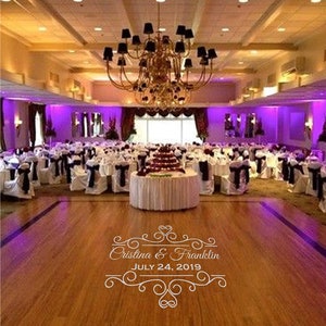 May include: A wedding reception venue decorated with purple lighting and white linens. The dance floor is empty and the tables are set with chairs. The text "Cristina & Franklin JULY 24, 2019" is printed on the floor.