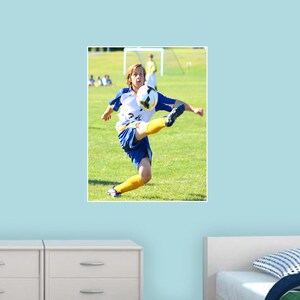 May include: A young person wearing a blue and yellow soccer uniform kicks a soccer ball in a field. The person is wearing yellow shin guards and blue cleats.