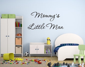Op de afbeelding: Kinderslaapkamer met een lichtblauwe muur met de tekst "Mommy's Little Man" in zwart schrift. De kamer bevat een wit bed, een groene stoel, een witte kast en speelgoed verspreid over de vloer.
