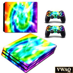 May include: A gaming console and two controllers with a vibrant tie-dye design in rainbow colours. The console and controllers feature a swirling pattern of blue, green, yellow, orange, and purple. The controllers are black with the tie-dye design on the touchpad.