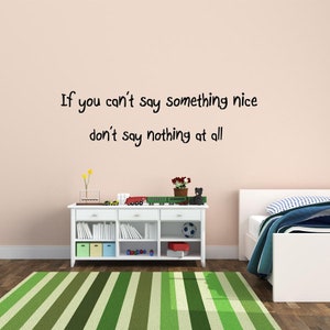 May include: A white wall with black text that reads "If you can't say something nice don't say nothing at all". The wall is in a room with a white dresser, a green and white striped rug, and a white bed with blue and white bedding.