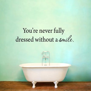 Puede incluir: Una bañera blanca con grifería cromada se encuentra frente a una pared verde claro con la cita "You're never fully dressed without a smile." escrita en ella.