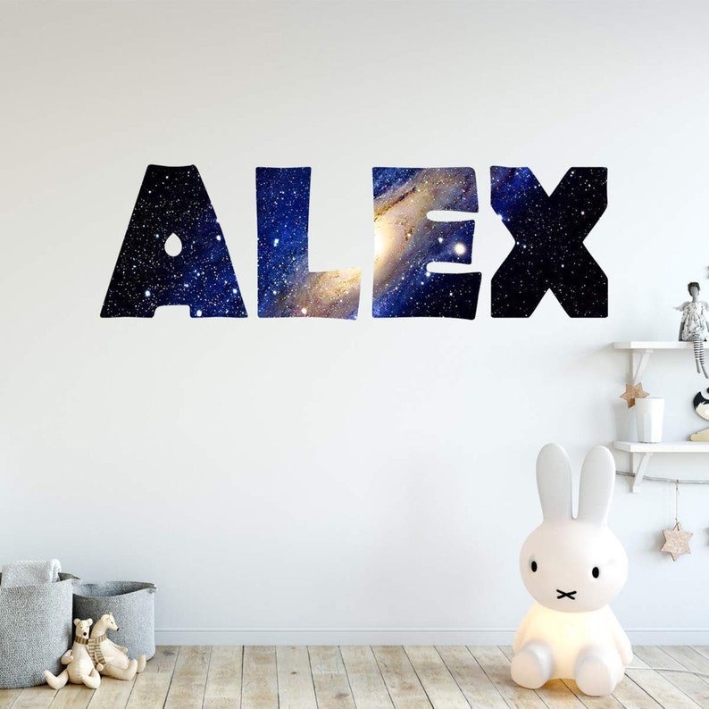 May include: A wall decal with the name "ALEX" spelled out in large, black letters. The letters are filled with a galaxy-themed pattern of blue, purple, and white.