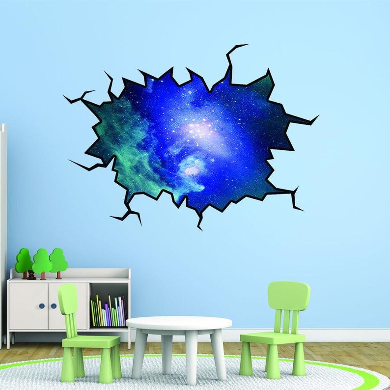 Pode incluir: Um adesivo de parede de gal&aacute;xia azul e verde com um efeito de parede rachada. O adesivo &eacute; aplicado em uma parede azul clara em um quarto com uma mesa branca e duas cadeiras verdes.