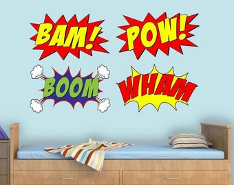 May include: Four colorful comic book style sound effects, "BAM!", "POW!", "BOOM", and "WHAM!" are displayed on a light blue wall above a wooden bed with a blue mattress and a striped blanket.