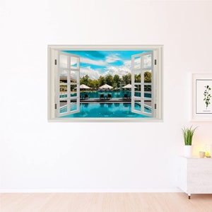 Puede incluir: Un marco de ventana blanco con ventanas abiertas que dan a una piscina con tumbonas y sombrillas. La piscina está rodeada de árboles verdes y un cielo azul con nubes blancas.