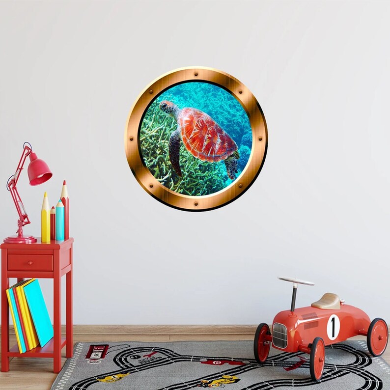 May include: A round, wooden-framed porthole sticker with a sea turtle swimming in a coral reef. The turtle is red, orange, and yellow, and the coral reef is blue and green.