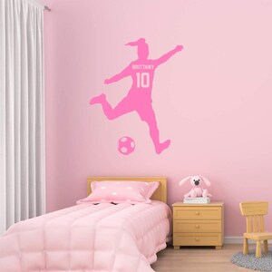 May include: Pink soccer player wall decal with the name "Brittany" and the number "10" on the jersey. The decal is shown on a pink wall in a bedroom setting.