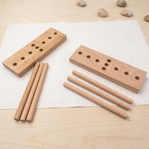 May include: Two wooden toy blocks with drilled holes and three wooden dowels. The blocks are rectangular and light brown. The dowels are cylindrical and also light brown. The blocks have different hole patterns.