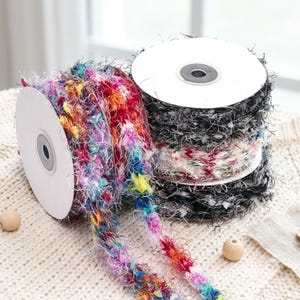 May include: Spools of colorful, textured ribbon in various colors, including rainbow, black, and floral patterns. The ribbon is wound on white cardboard spools, ideal for crafting and decorative projects.