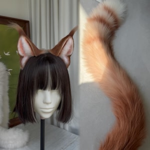 Op de afbeelding: Een set kunstbont dierenoren in bruin- en wittinten, bevestigd aan een haarband, gepresenteerd op een etalagepophoofd met een donkerbruine bob-pruik. Een lange, bijpassende kunstbont dierenstaart in oranje en witte kleurverloop staat verticaal.