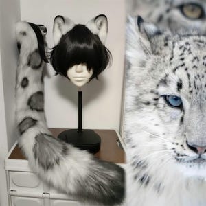May include: A snow leopard-themed costume set featuring a faux fur tail and cat ear headband. The tail is white with grey spots and a grey tip. The headband has white ears with black tips. A mannequin head with a black wig is also present.