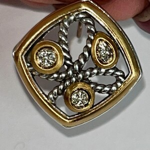 K&ouml;nnte beinhalten: Quadratischer Ohrring mit goldfarbenem Rahmen und silberfarbenem Seildesign. Der Ohrring hat drei goldfarbene Kreise mit funkelnden, klaren Steinen. Der Ohrringstift ist sichtbar.