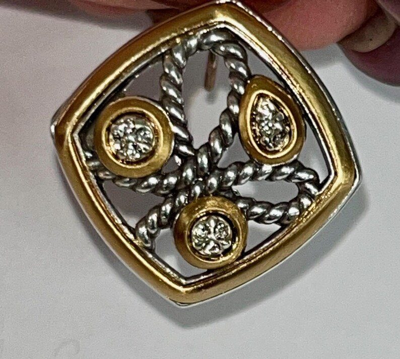 K&ouml;nnte beinhalten: Quadratischer Ohrring mit goldfarbenem Rahmen und silberfarbenem Seildesign. Der Ohrring hat drei goldfarbene Kreise mit funkelnden, klaren Steinen. Der Ohrringstift ist sichtbar.